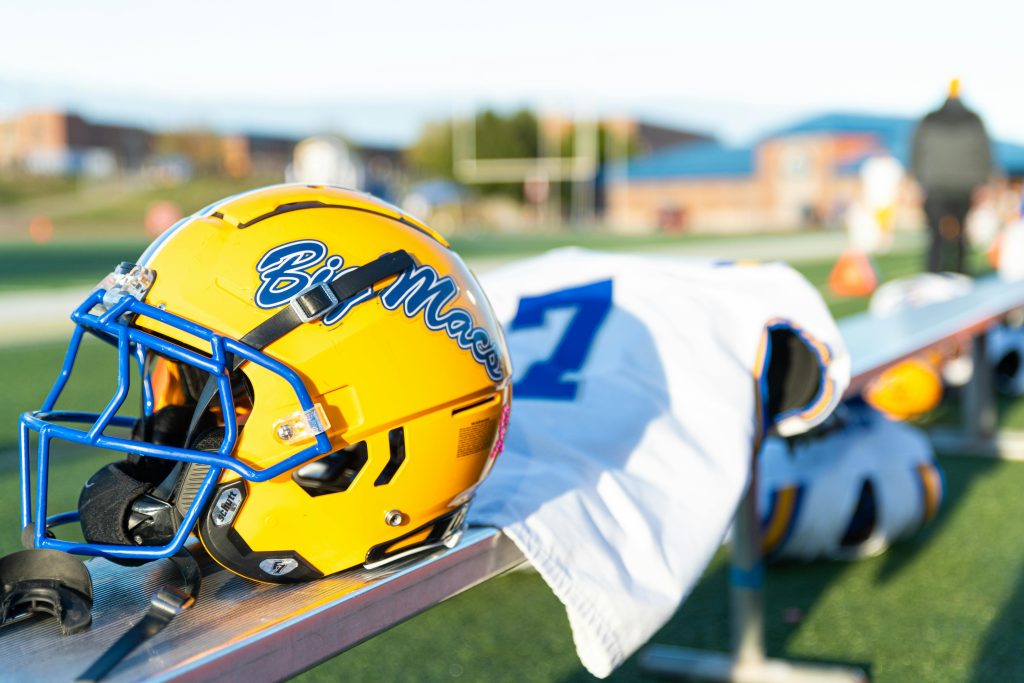 A yellow football helmet with blue highlights rests on a sports bench, ready for the game.